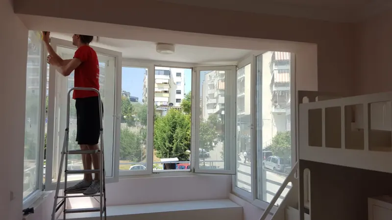 Punonjës i Ndihma Plus duke pastruar dritaret e një apartamenti në Tiranë